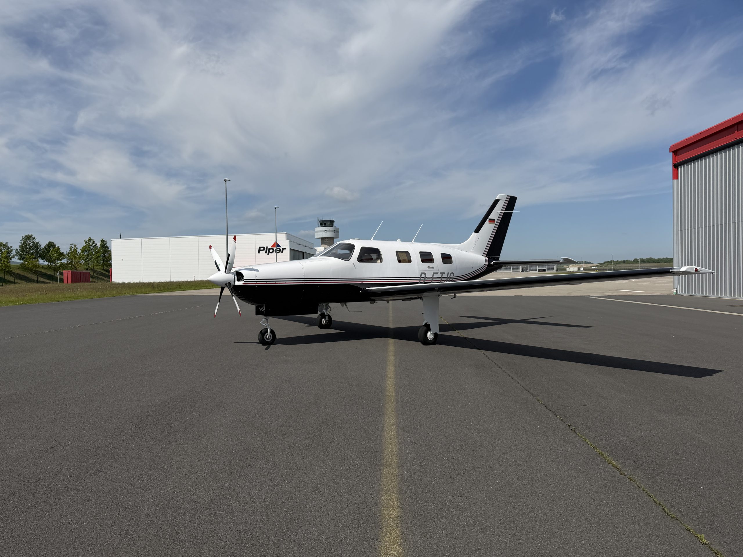 Ansicht von vorne links einer weiß-schwarzen Piper Mirage von 1992. Die Maschine steht auf einem Flugplatz unter leicht bewölkten Himmel.